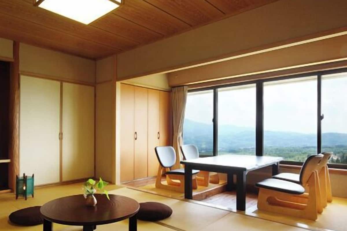 Une pièce de style japonais traditionnel, avec un sol recouvert de tatamis, une table basse avec des coussins et une vue sur les montagnes par de grandes fenêtres.
