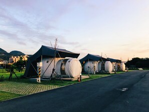 A row of cylindrical tents with a flat roof, arranged along a paved road with a grassy area in front.