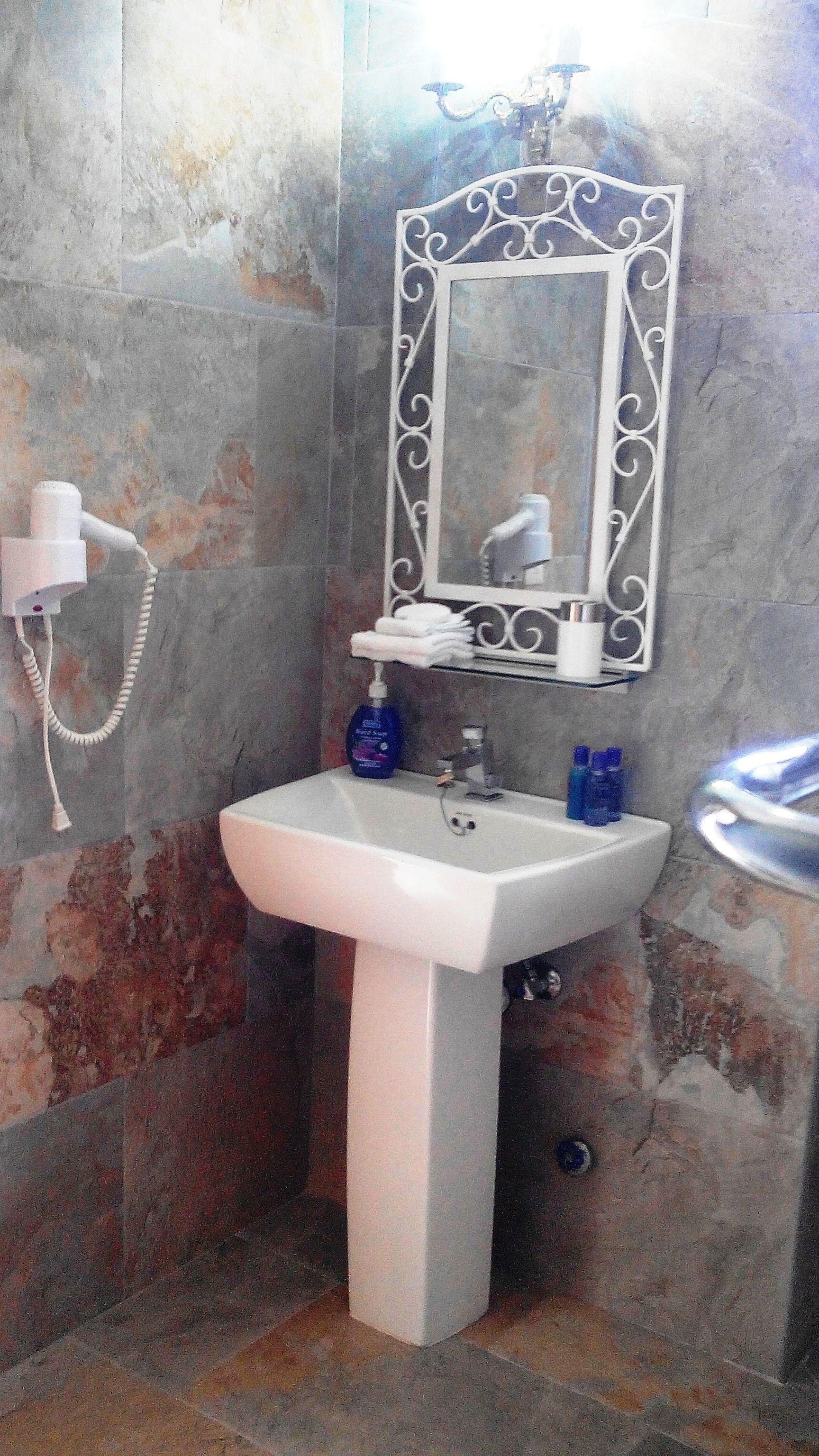 A bathroom with a white pedestal sink, a mirror with ornate metal framing, and a towel rack.