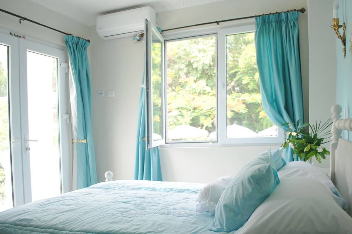 A bedroom with a bed, curtains, a window, and a wall-mounted air conditioning unit.