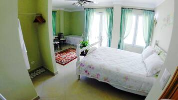 Un dormitorio con una cama, un ventilador de techo, una ventana con cortinas y un pequeño escritorio con silla.