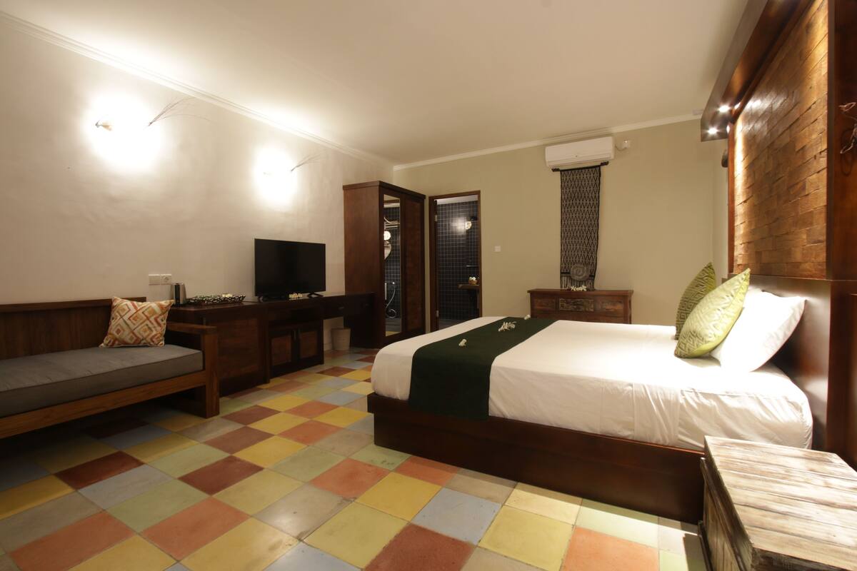 A hotel room with a bed, a sofa, a TV, and a bathroom visible through an open door.