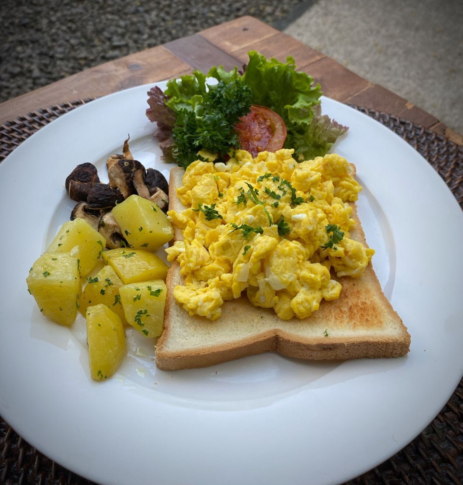 A plate with scrambled eggs, toast, potatoes, mushrooms, lettuce, and a tomato.