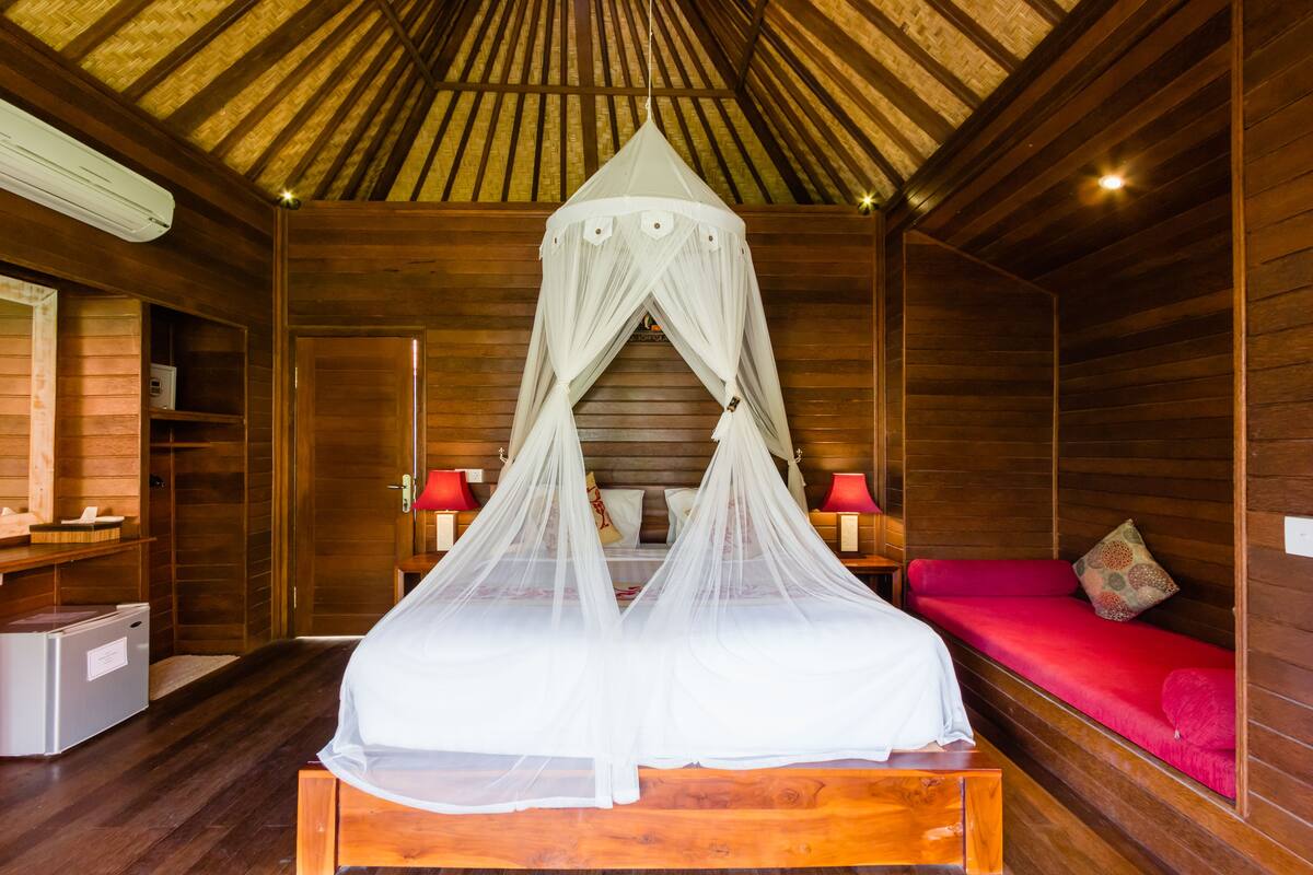 Une pièce avec un plafond en bois, un lit à baldaquin, un canapé rouge et une petite table avec une lampe.