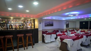 A bar area with a variety of liquor bottles and stools, and a dining area with tables set for a meal. - Hotel Shivam Plaza (Kathmandu)