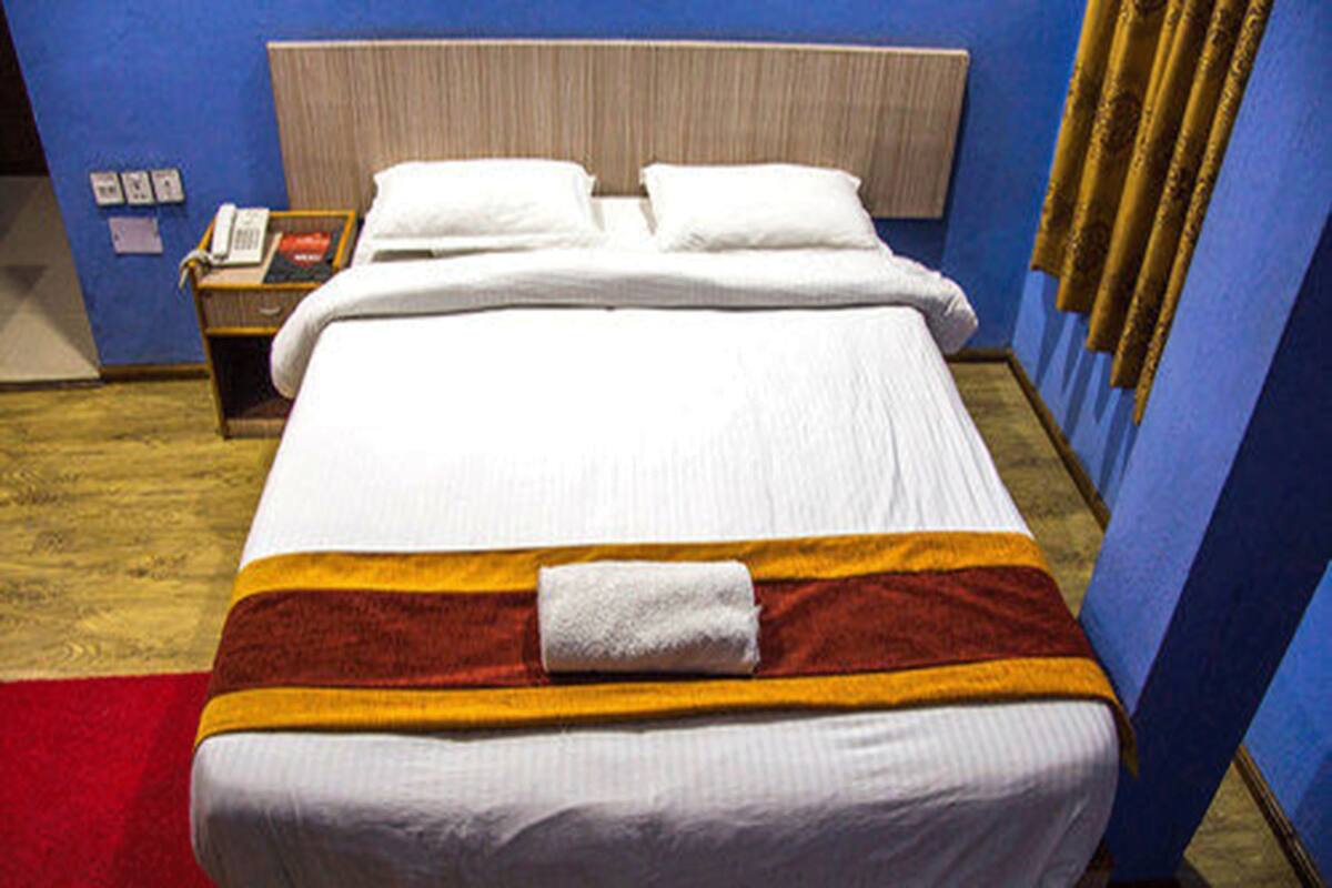 A hotel room with a bed, a nightstand with a phone, and a red carpet.