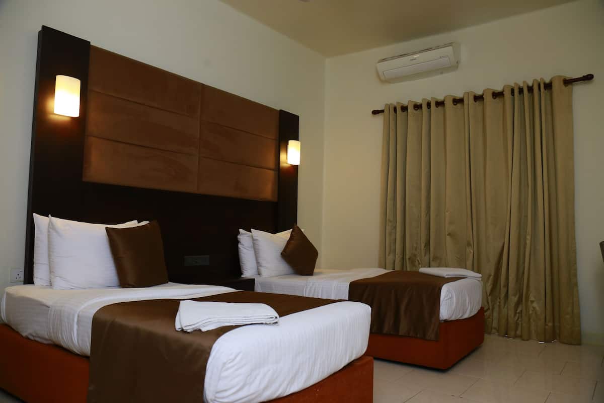 A hotel room with two beds, a wooden headboard, a wall-mounted air conditioner, and beige curtains.