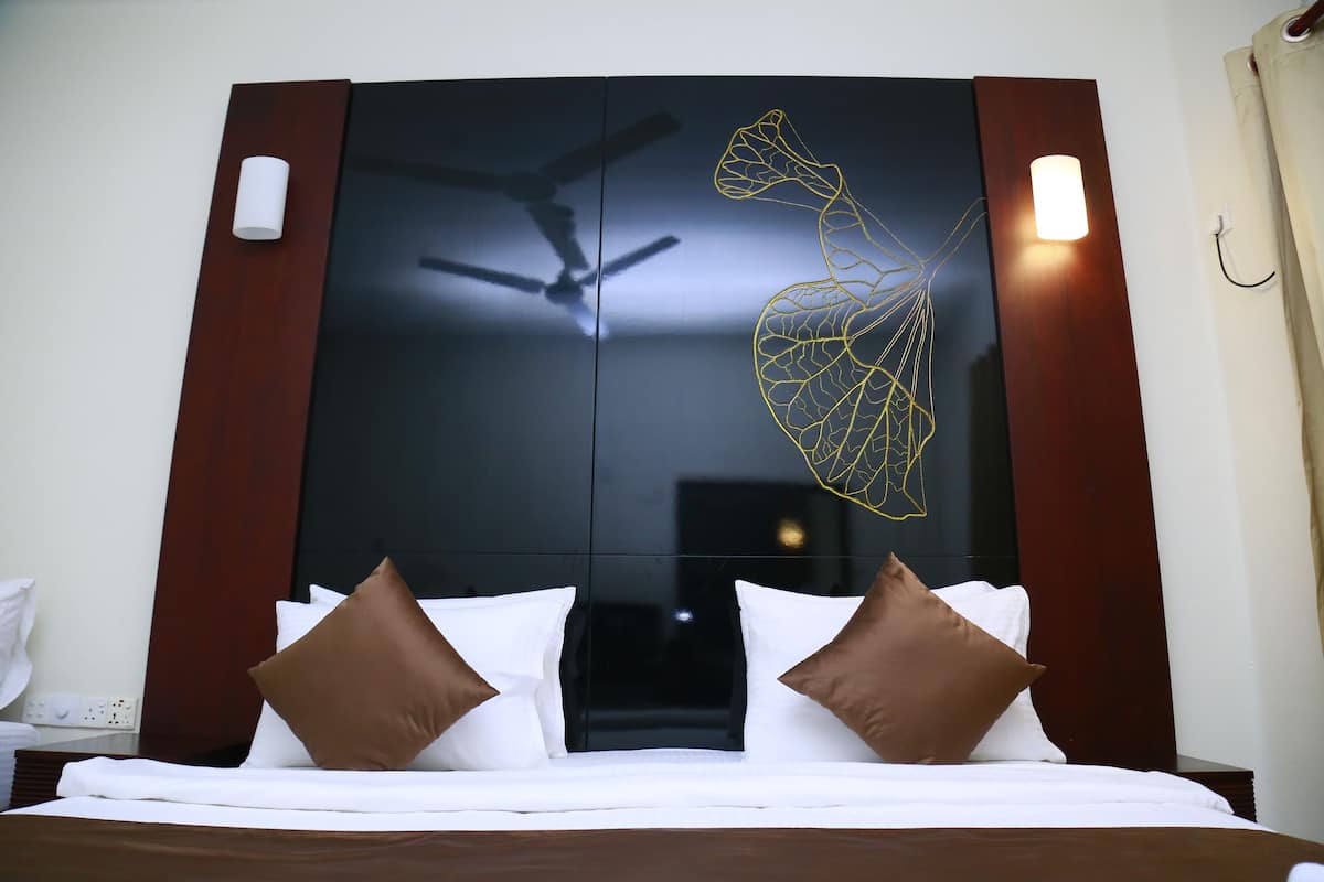 A hotel room with a bed, a ceiling fan, and a wall-mounted light fixture.