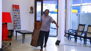 A man carrying a suitcase in a room with a bookshelf, a red lamp, and a bench. - Sea port hotel (Negombo)