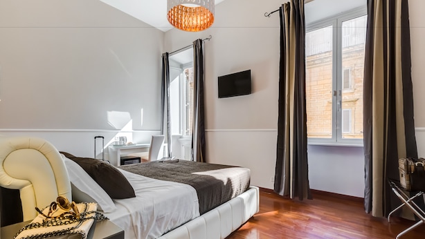 A modern bedroom with a bed, a chair, a desk, and a TV. - Relais Vatican Suites (Rome)