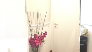 A hallway with a wooden floor, a white door, and a vase with pink flowers. - Relais Vatican Suites (Rome)