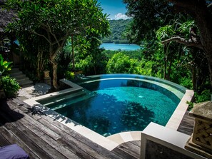 Una piscina azul cristalina rodeada de exuberante vegetación y una terraza de madera.