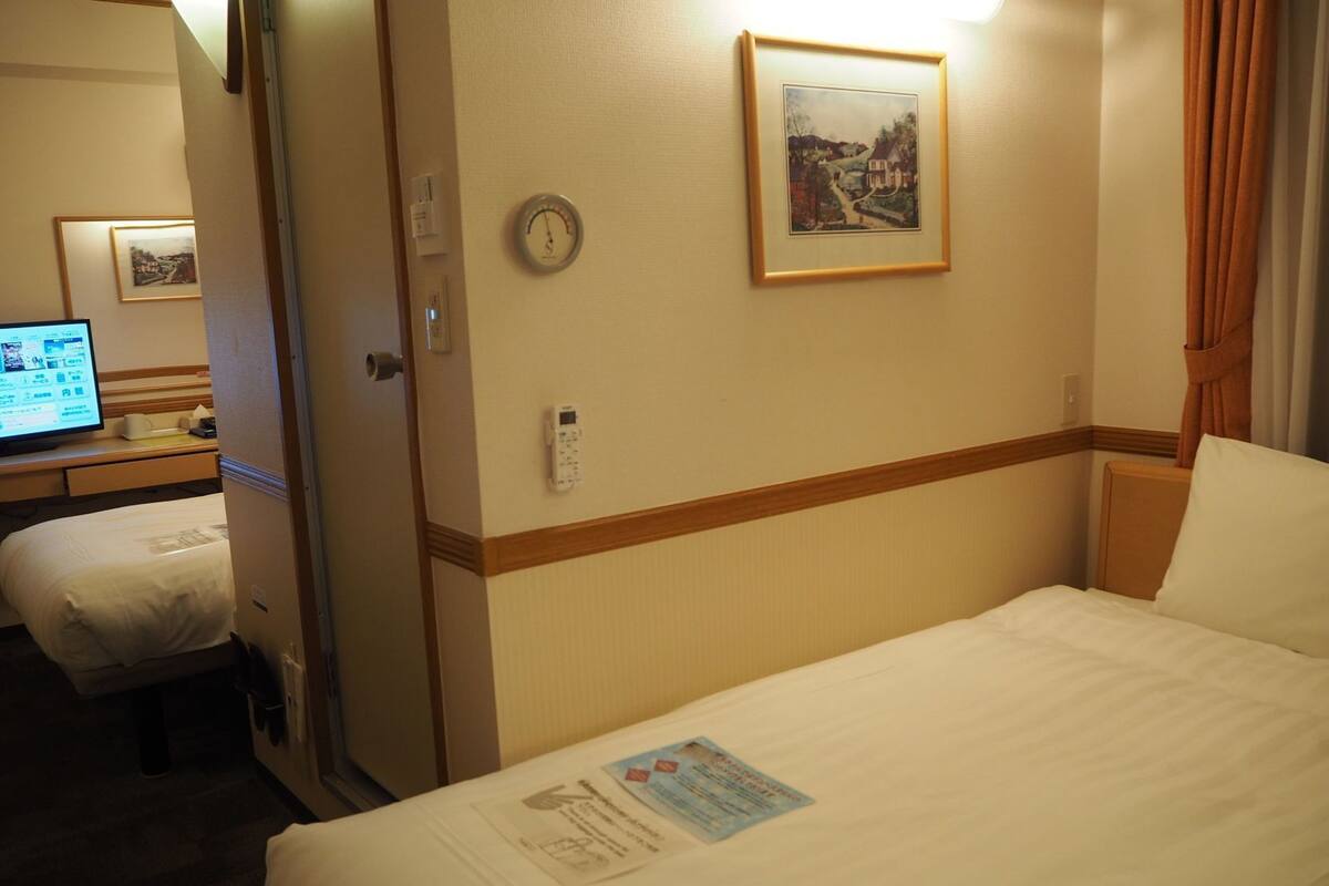 A hotel room with a bed, a desk with a computer, a clock, and a framed picture on the wall.