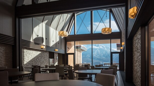 Un comedor moderno con ventanas amplias, mesas de madera y vistas a montañas.