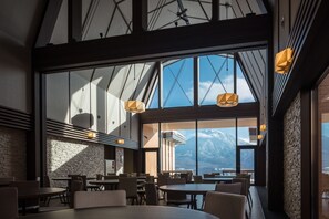 A modern dining area with large windows, wooden tables, and a view of mountains. - Niseko Hakuunso (Kutchan)