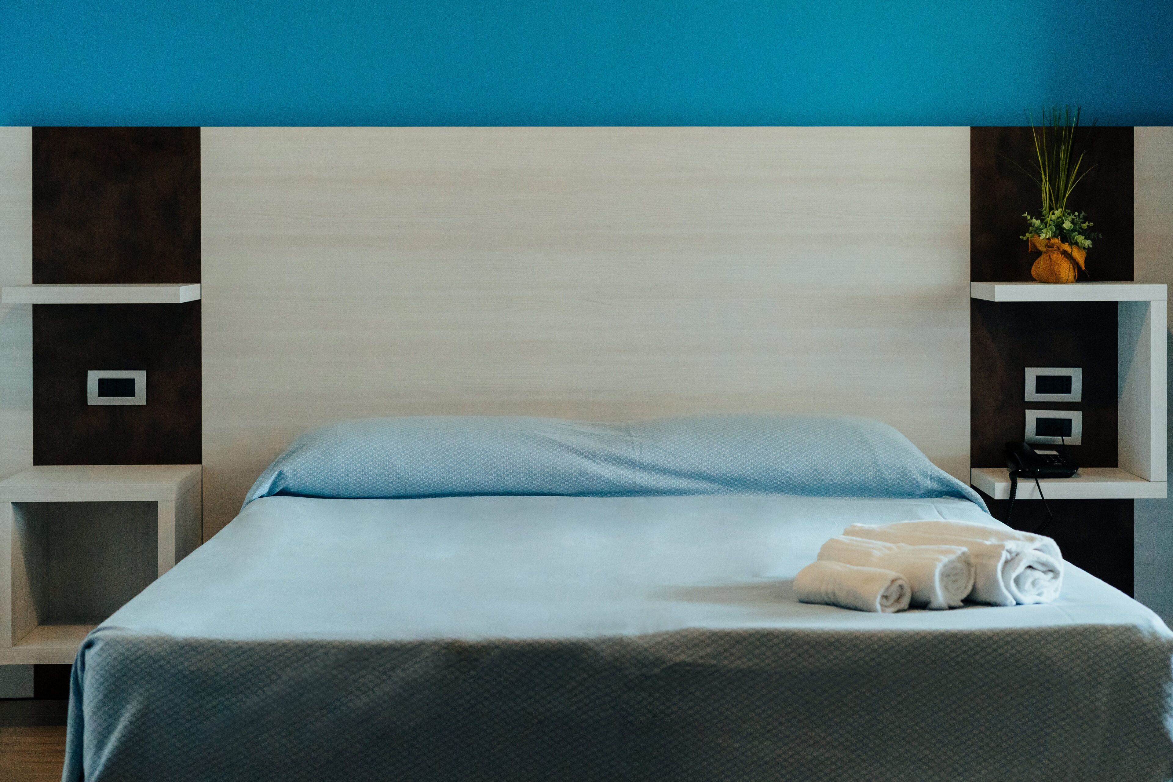 A hotel room with a bed, a nightstand, a wall-mounted shelf with a plant, and a telephone.