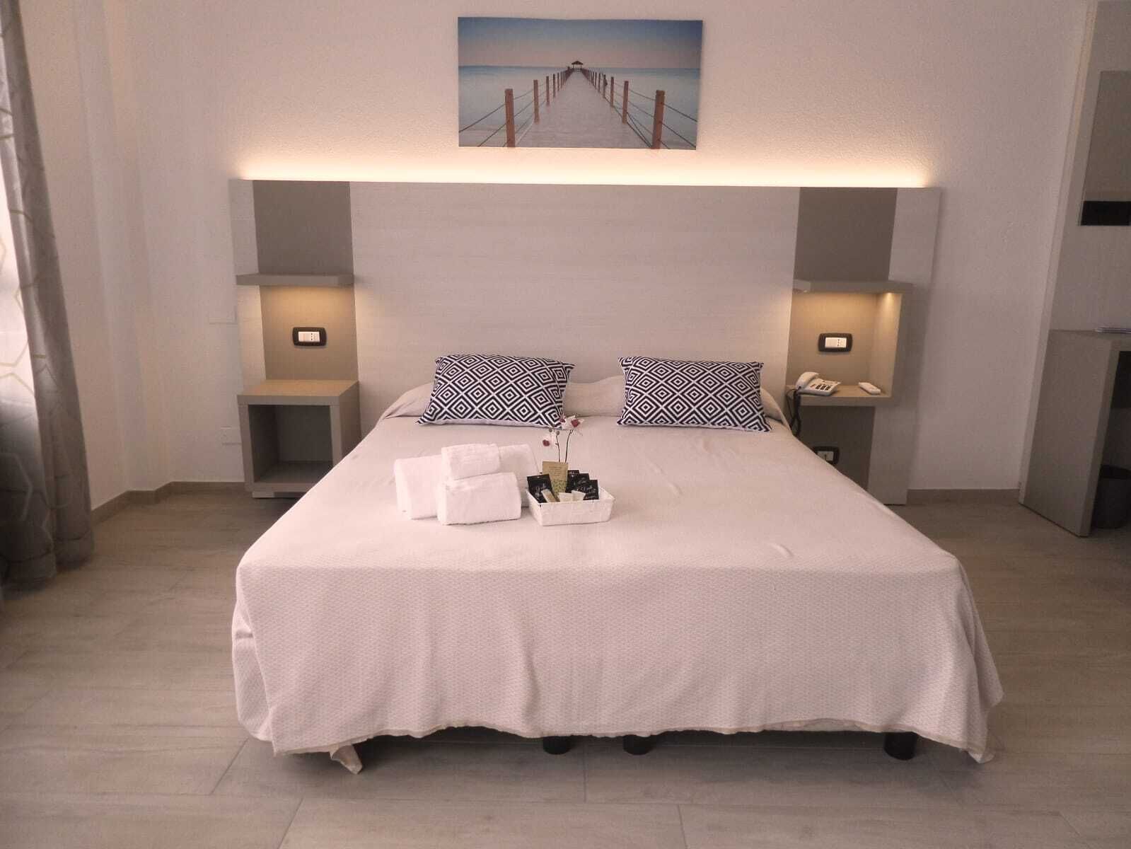 A neatly made bed with white linens, two bedside tables with lamps, and a painting above the bed.