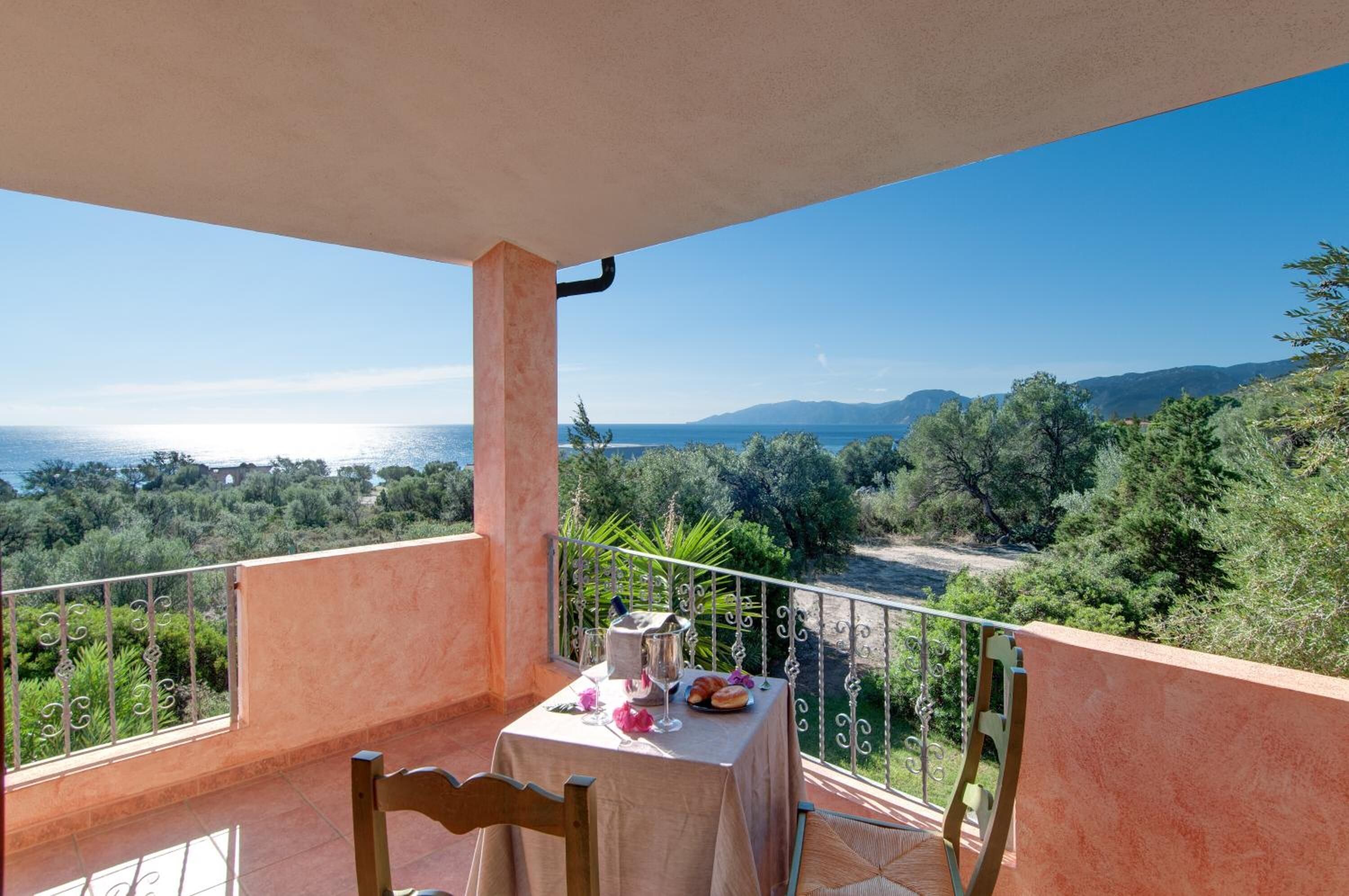 A balcony with a table set for two, overlooking a scenic view of the sea and mountains.