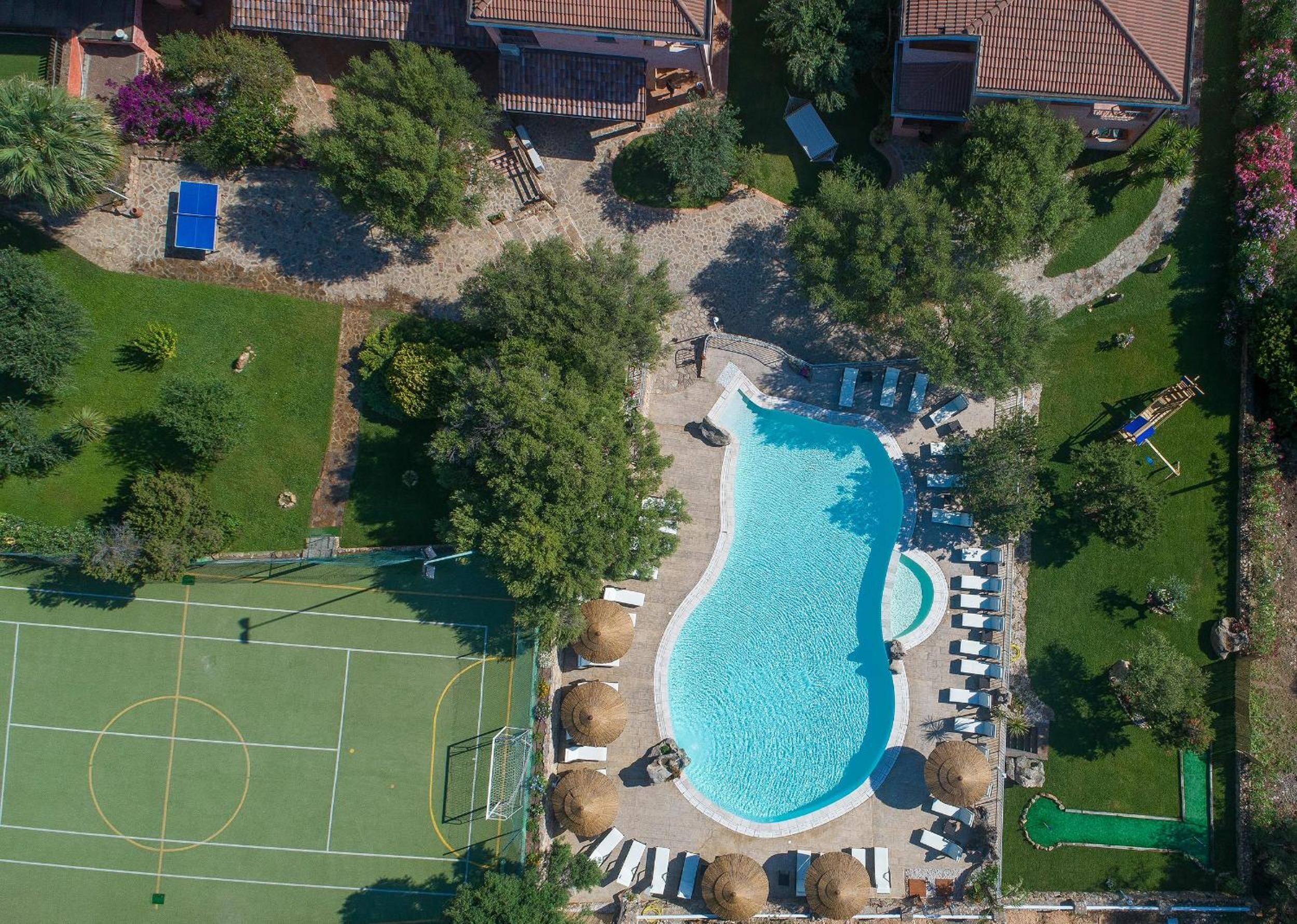 An aerial view of a residential area with a swimming pool, a tennis court, and a garden.