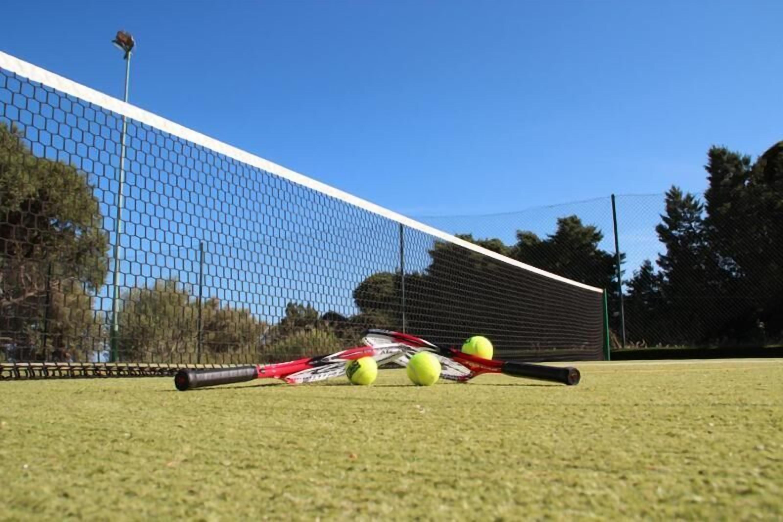 En tennisbane med net, tennisraketter og bolde.