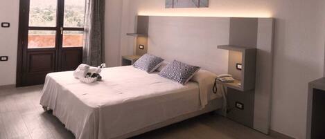 A neatly arranged bedroom with a bed, bedside tables, a painting, and a view through the window.