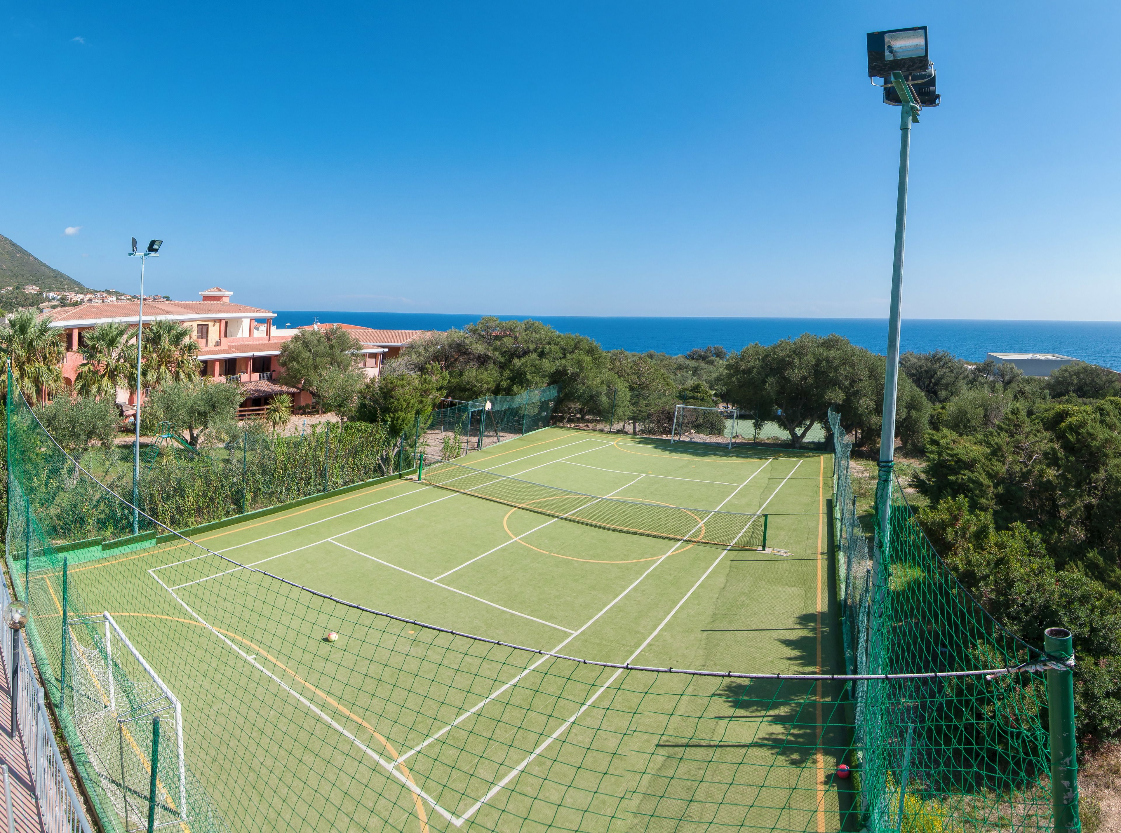 Ein Tennisplatz mit Netz, umgeben von Grünflächen und freiem Blick auf das Meer.