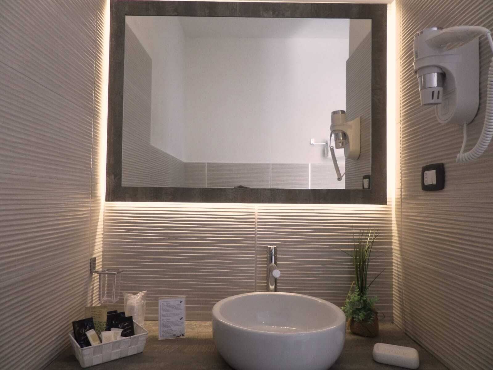 A modern bathroom with a large mirror, a round sink, and a hairdryer mounted on the wall.