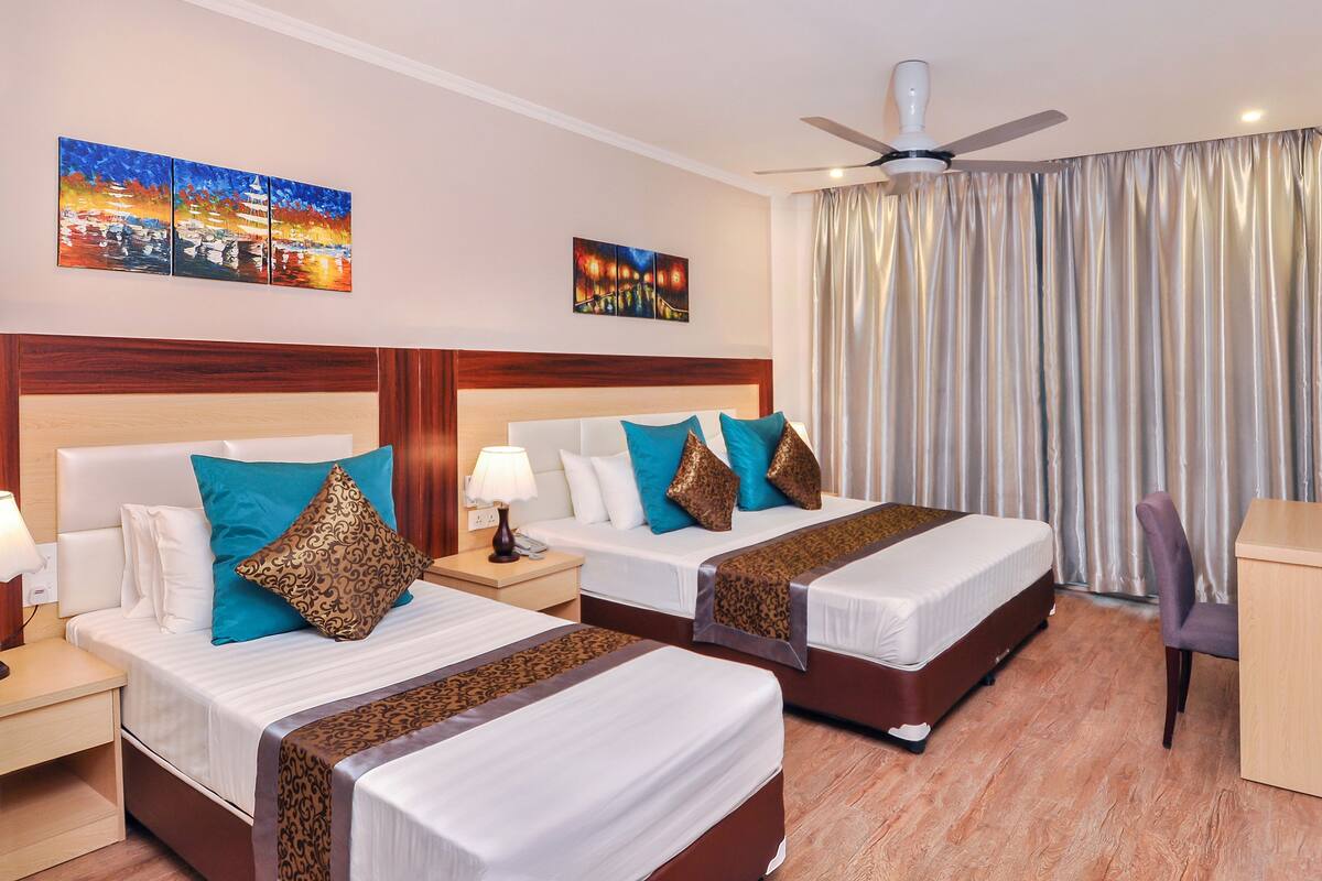 Quarto de hotel com duas camas, uma escrivaninha, uma cadeira, televisão e obras de arte nas paredes.