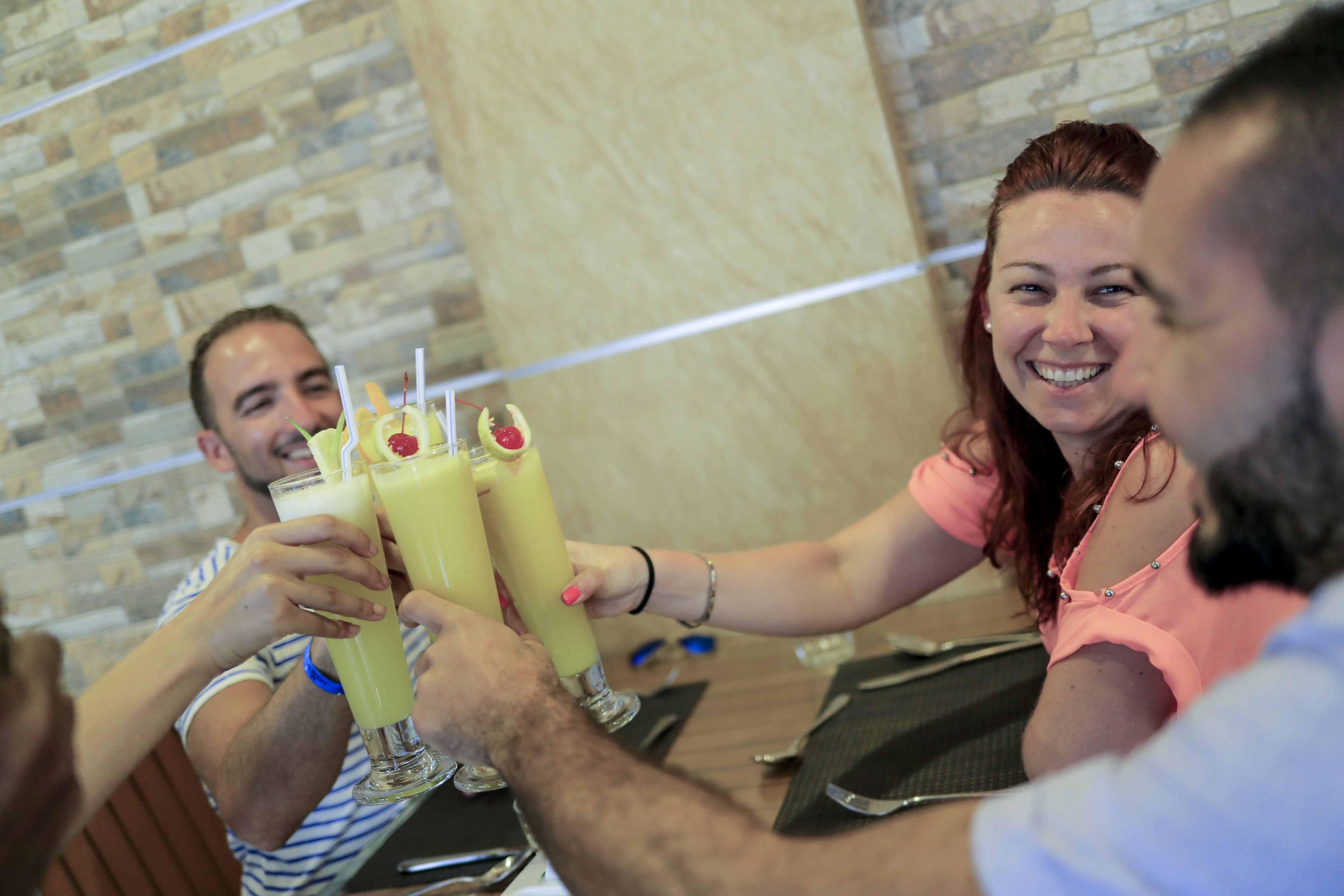 A group of people toasting with drinks at a table in a restaurant with a brick wall background.