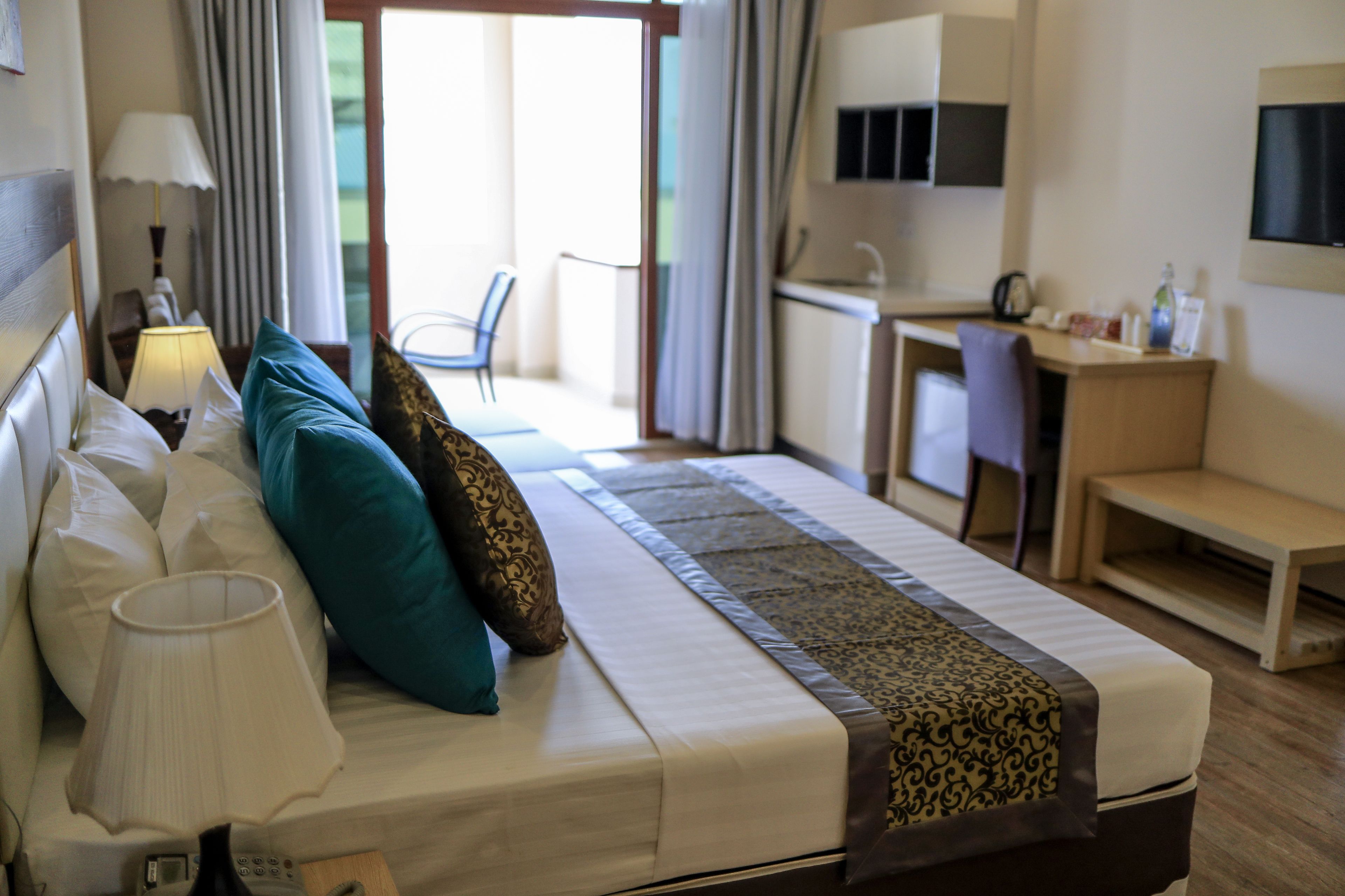 Una habitación de hotel con cama, escritorio, silla, televisión y lámpara.