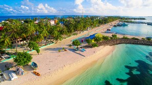 A beach with clear turquoise waters, palm trees, and a few boats. - Triton Beach Hotel & Spa (Maafushi)