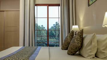 A hotel room with a bed, two pillows, a nightstand with a lamp, and a view through a window with curtains.