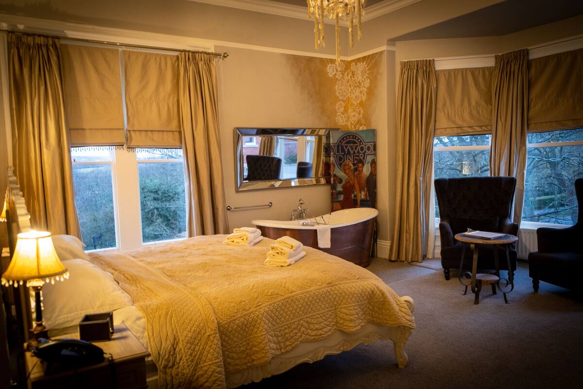 Hotelkamer met een groot bed, een zithoek met een fauteuil, een kaptafel met spiegel en een bad.