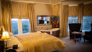 A hotel room with a large bed, a sitting area with a chair, a vanity with a mirror, and a bathtub.