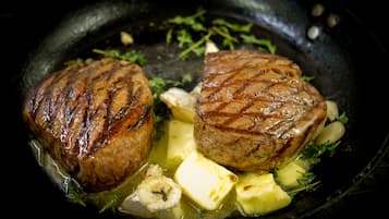 Duas bifanas grelhadas com batatas e ervas numa frigideira.