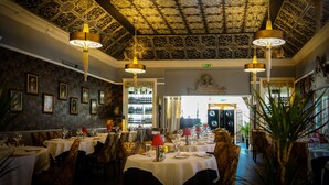 Een restaurant met een versierd plafond, kroonluchters en uitzicht op de straat.