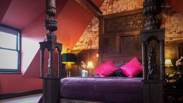 A four-poster bed with a purple bedspread, a wooden headboard, and a red pillow.