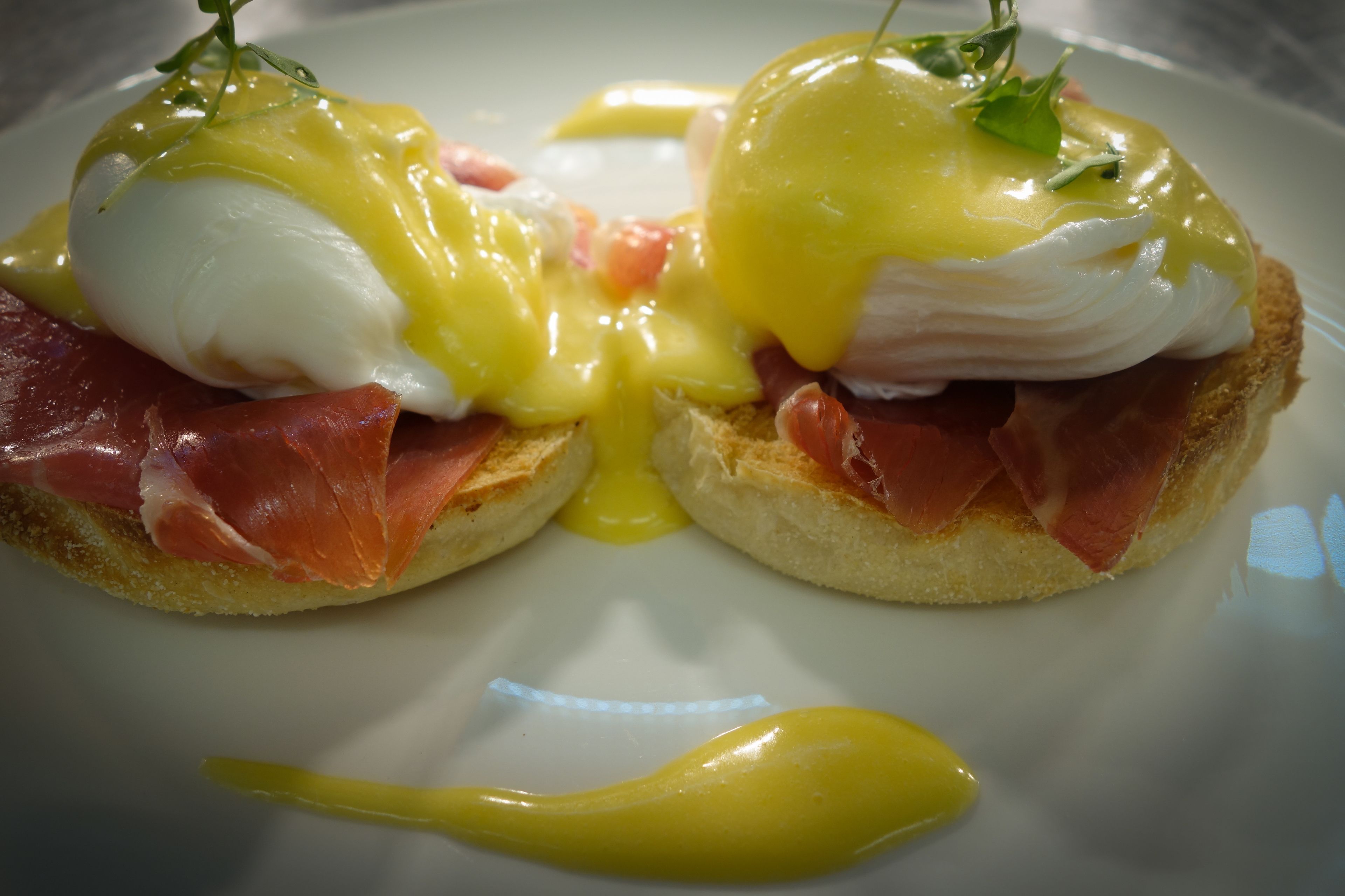 A breakfast dish with poached eggs, hollandaise sauce, and prosciutto on toast.