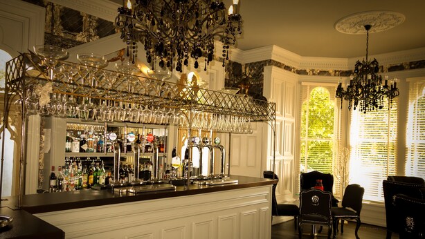 Een bar met een witte toonbank, flessenrekken en een kroonluchter.