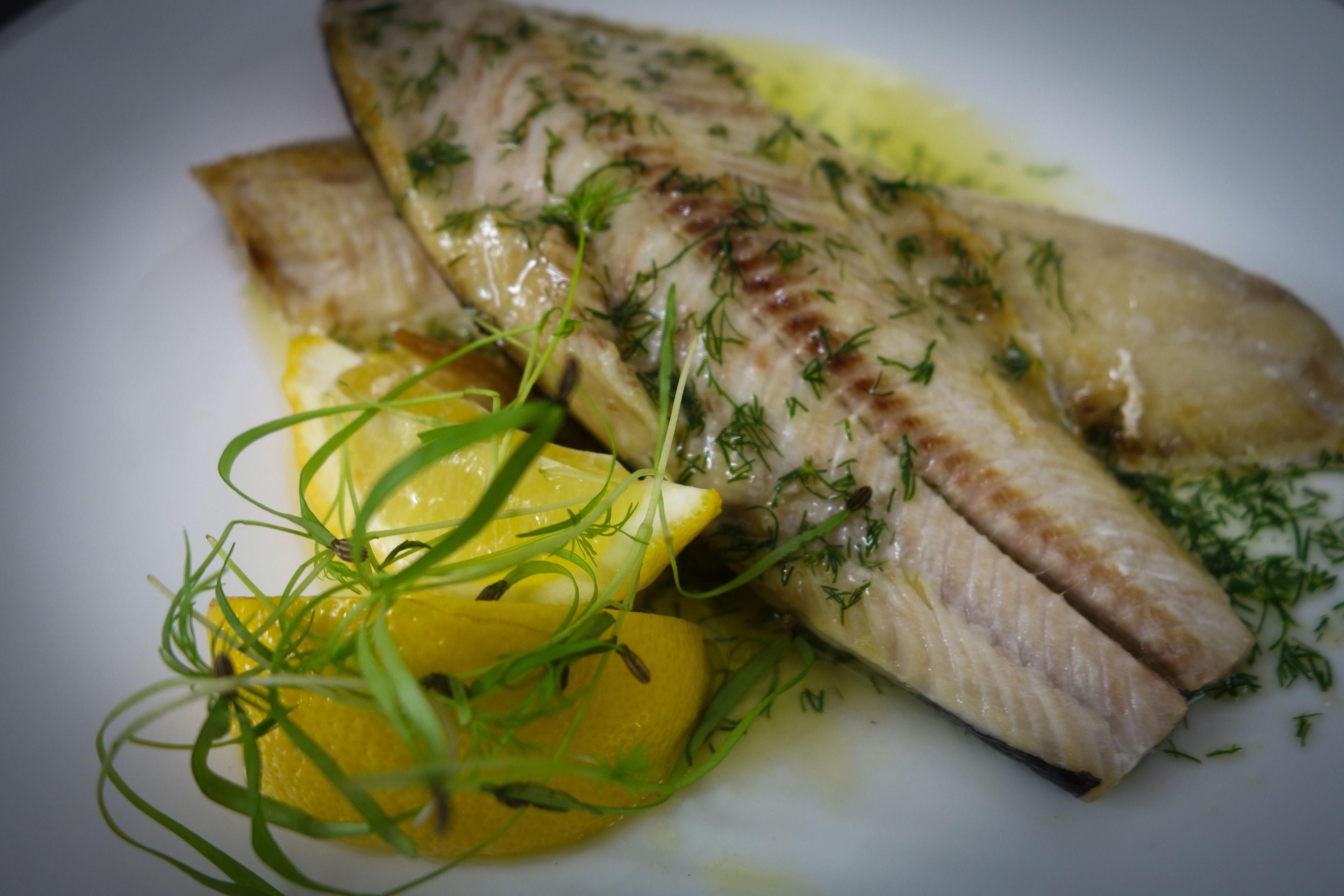 Un plato con un filete de pescado, rodajas de limón y hierbas verdes.