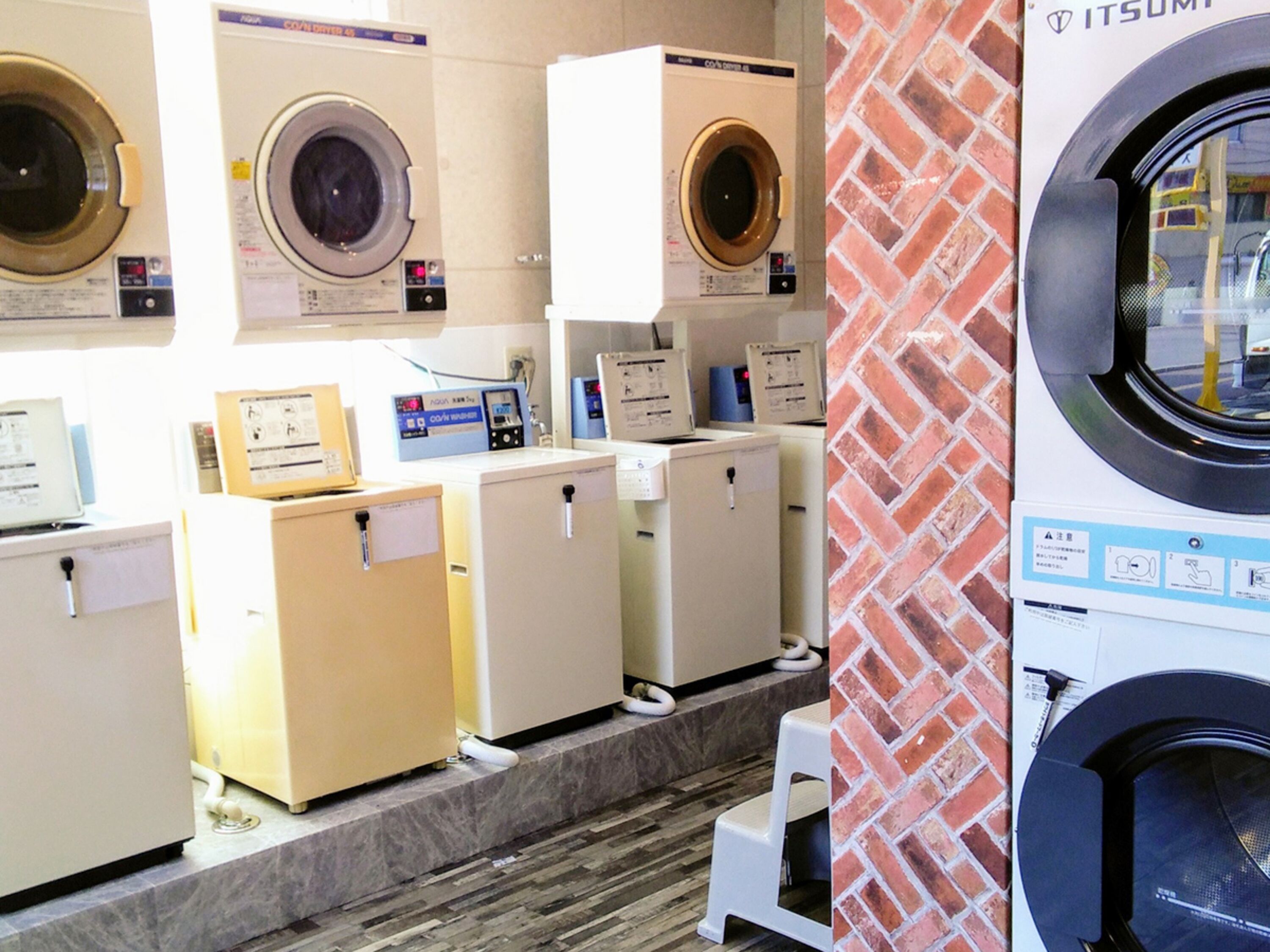 A laundromat with multiple washing machines and dryers, a tiled floor, and a brick wall.