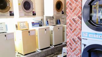 A laundromat with multiple washing machines and dryers, a tiled floor, and a brick wall.