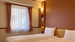 Una habitación de hotel con dos camas, una ventana con cortinas translúcidas, una lámpara fijada a la pared y un pequeño estante con un cuadro.