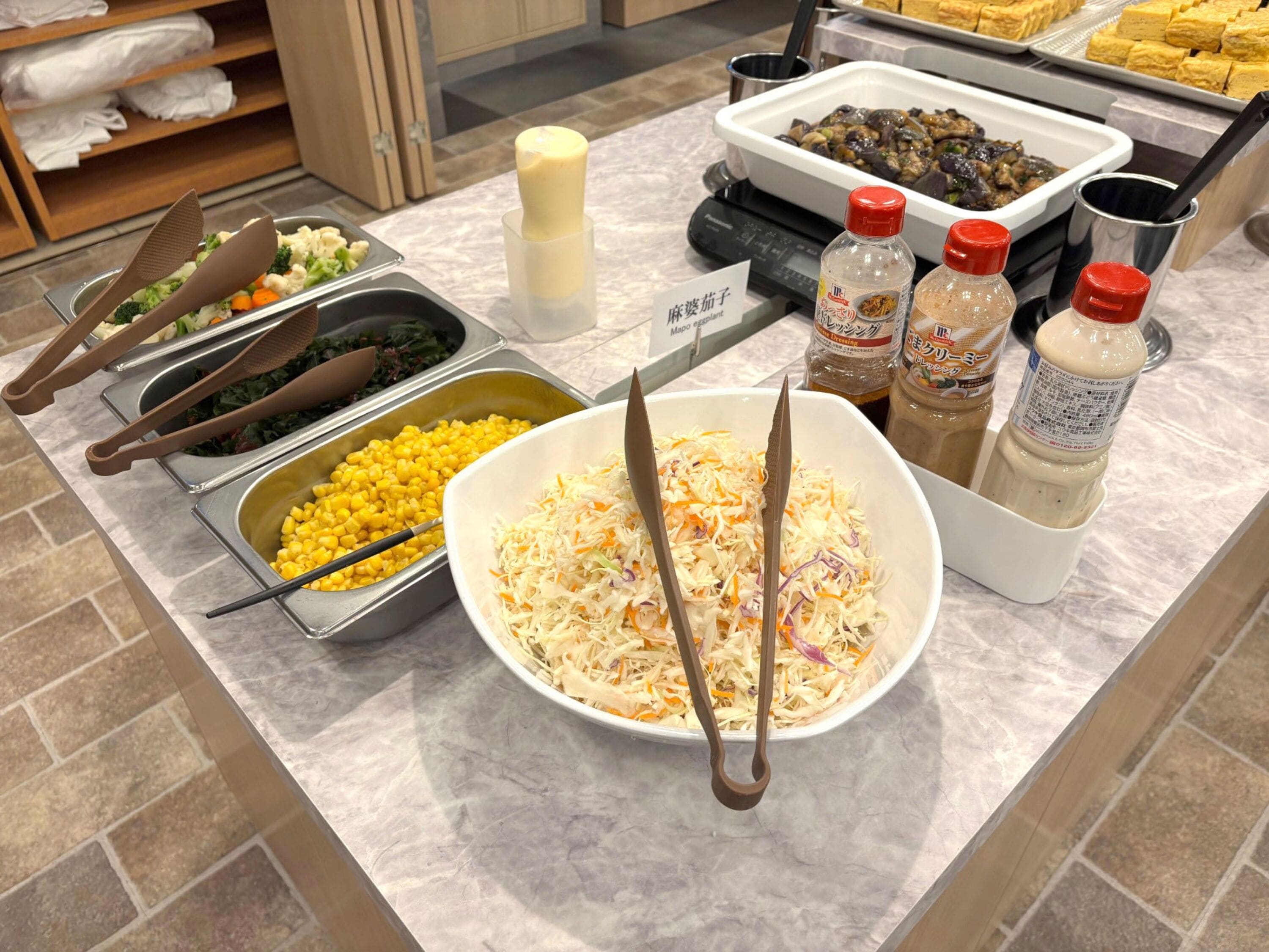 A buffet with various food items including coleslaw, corn, and mixed vegetables.