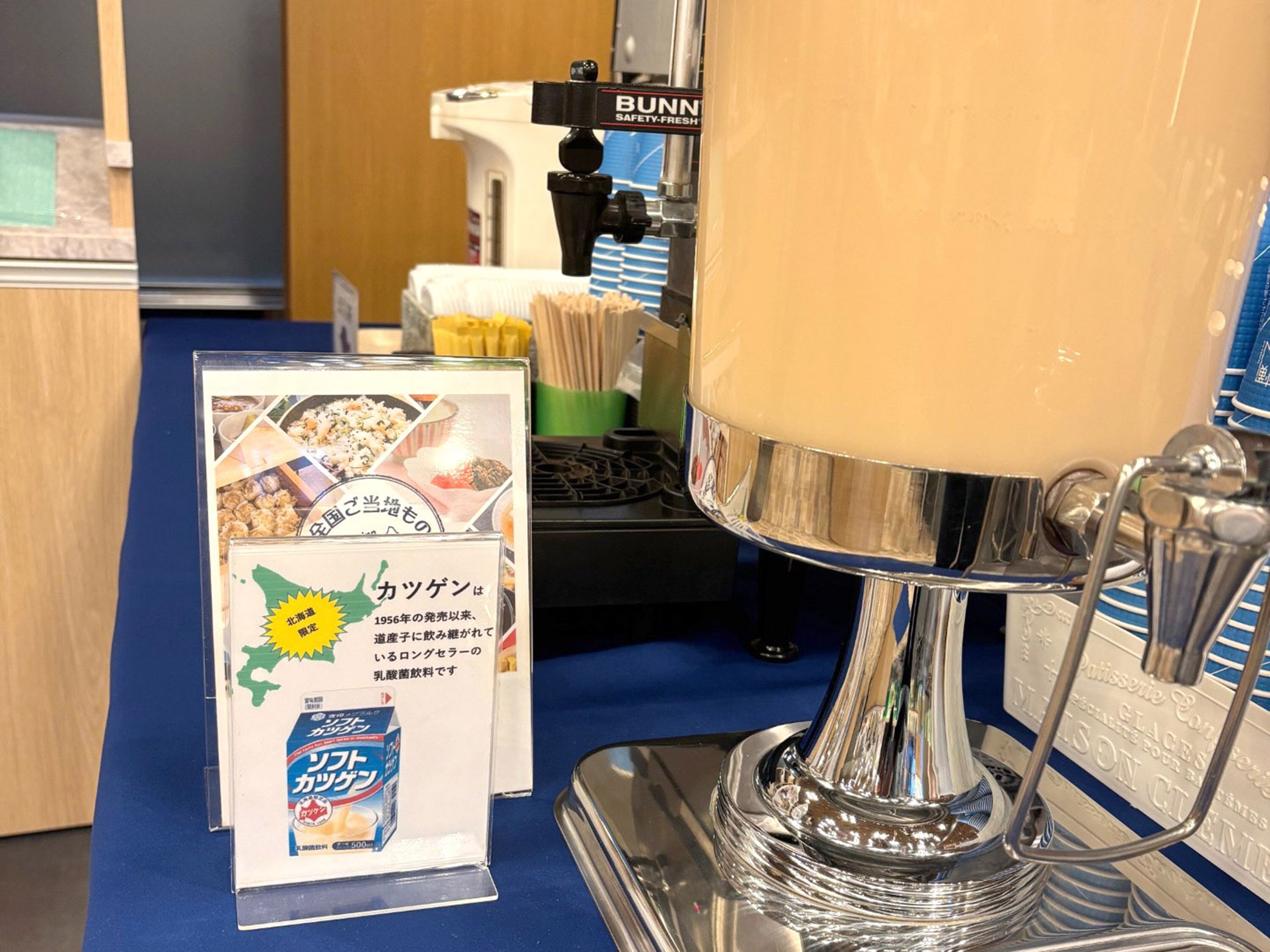 A coffee machine with a clear glass container, a signboard with Japanese text, and a blue counter.