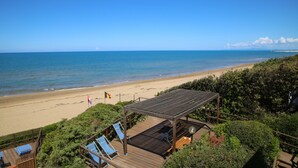 Blick auf einen Strand mit einer Holzterrasse, Liegestühlen und einem Pavillon mit Meerblick.