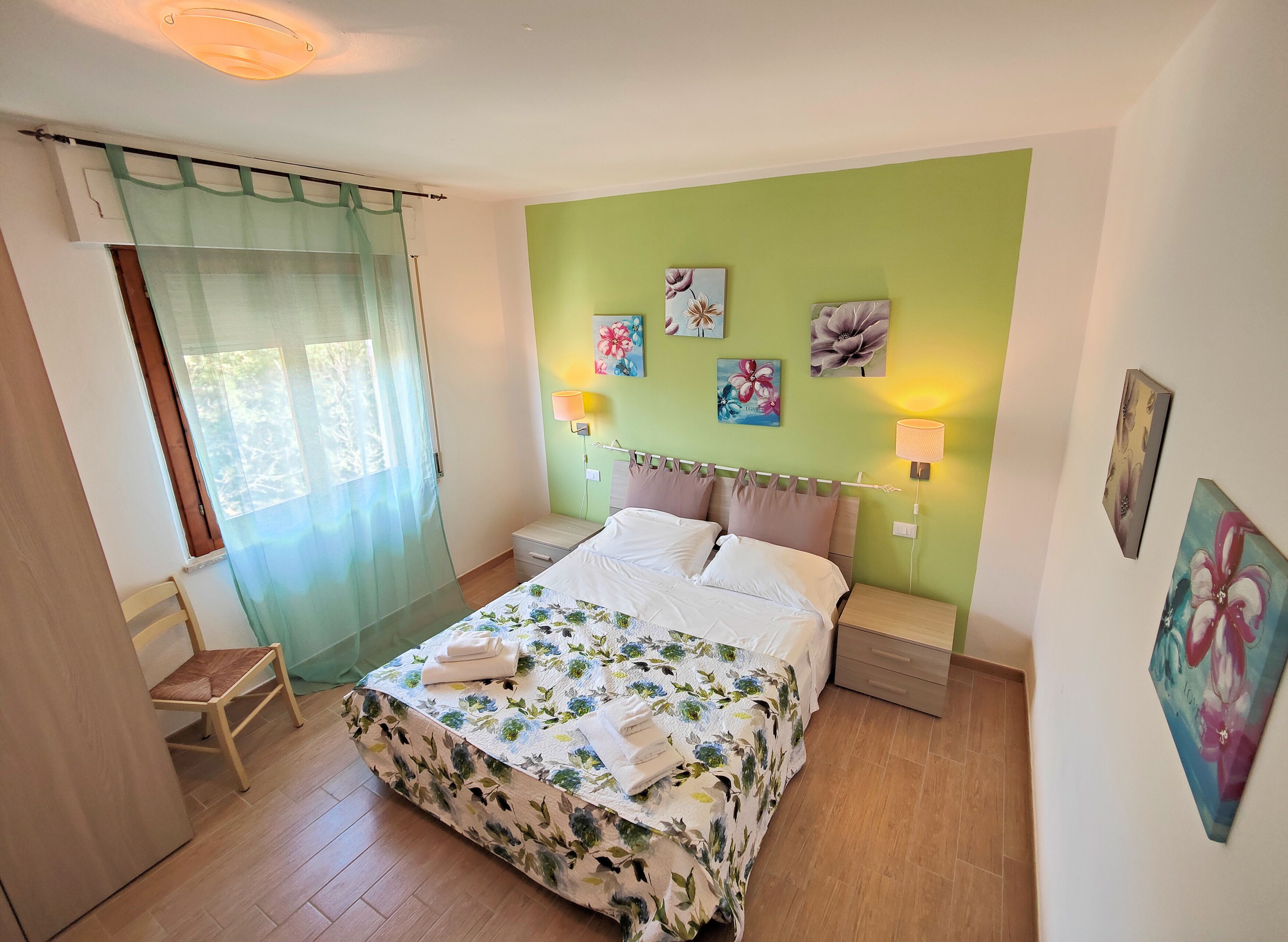 A bedroom with a bed, a chair, a nightstand, and wall art.