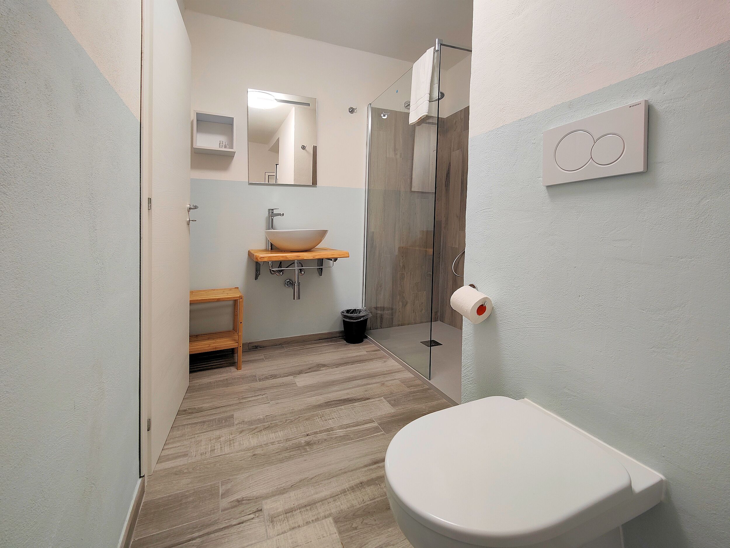 Une salle de bain moderne équipée de toilettes, d’un lavabo, d’une douche et d’une étagère en bois.