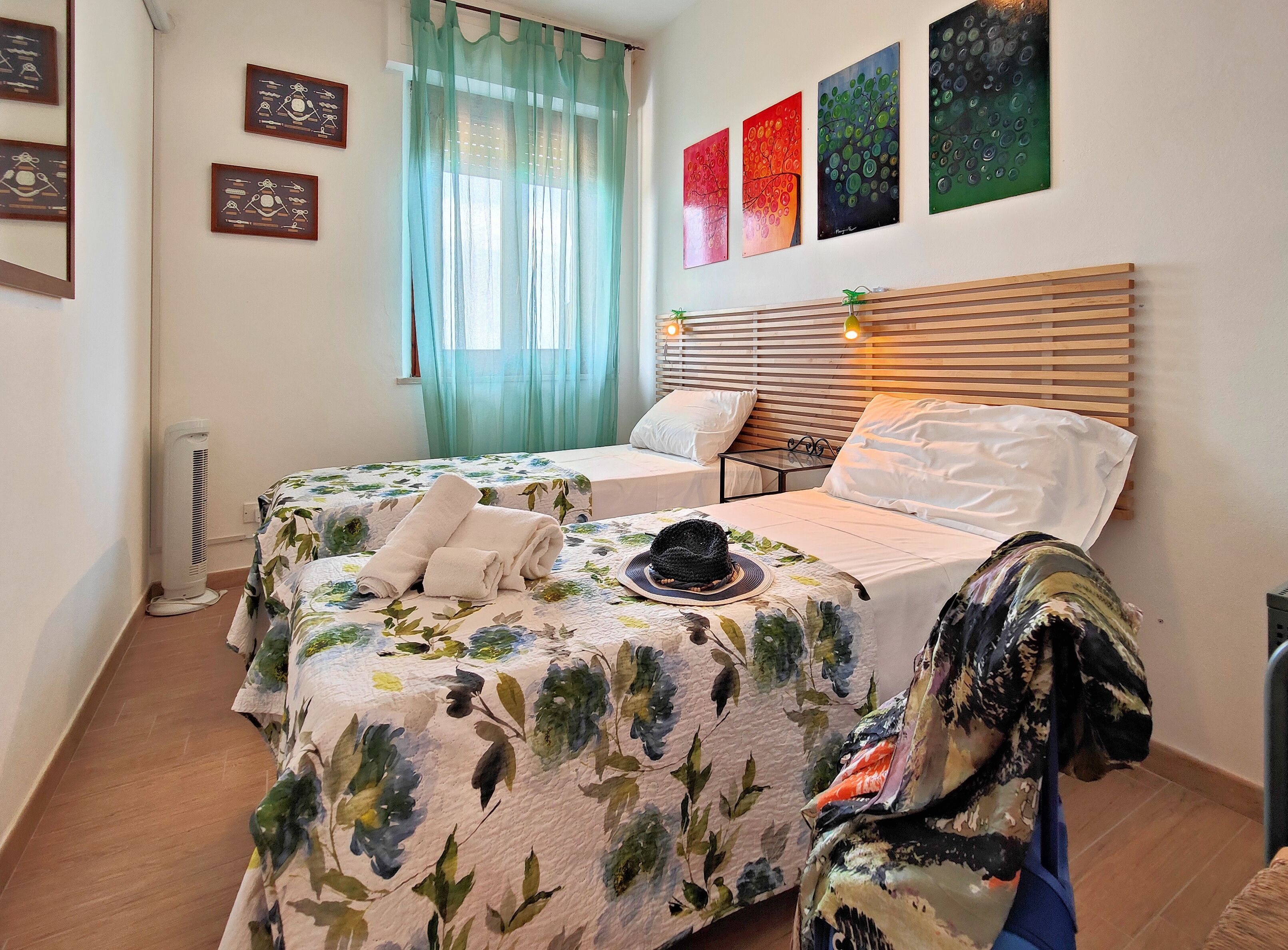 A bedroom with two beds, a window with sheer curtains, and a wall with four framed artworks.