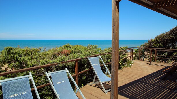 Eine Holzterrasse mit Liegestühlen, beschriftet mit "FUTURA CAY", mit Blick auf das klare, blaue Meer.